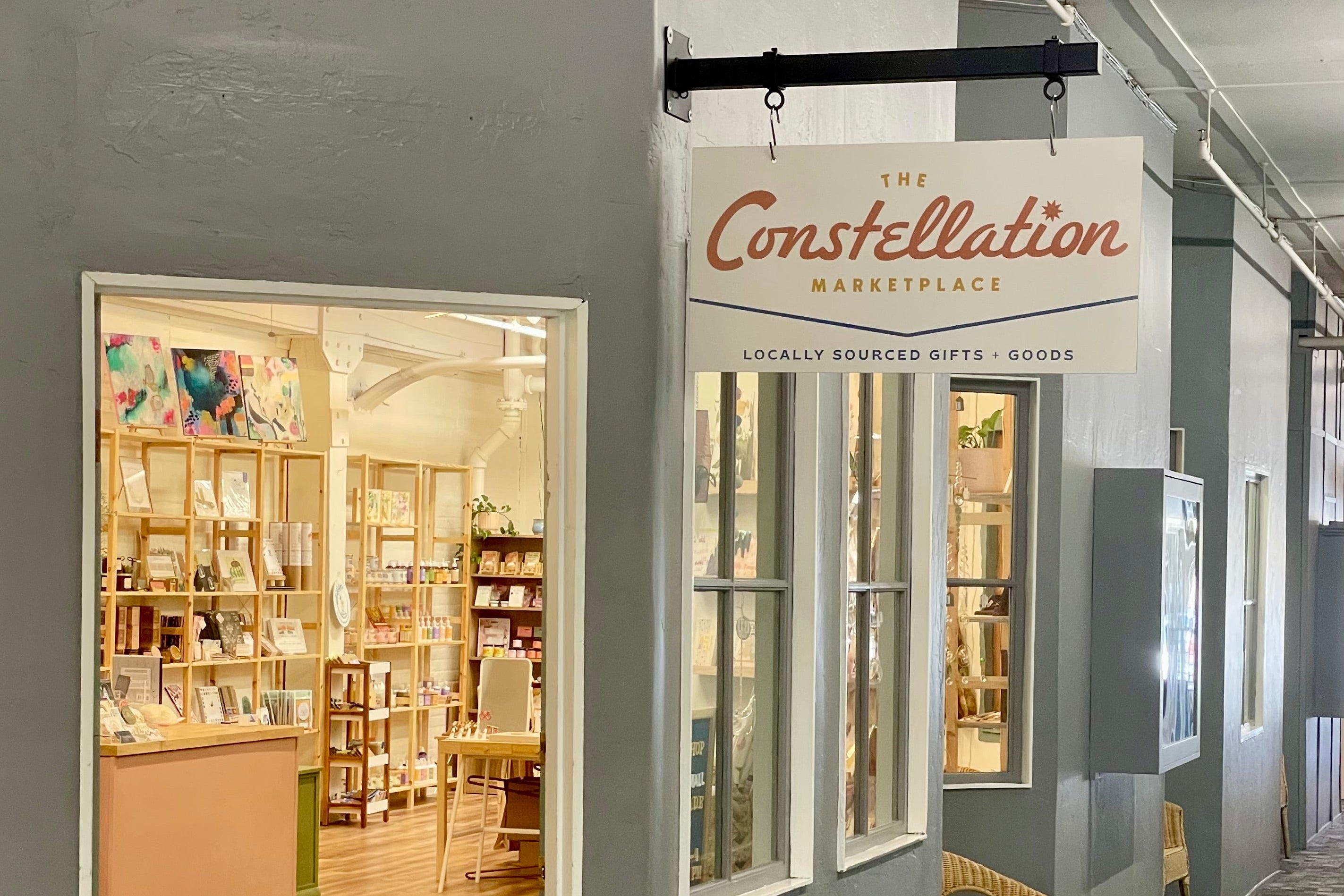 Interior of a store with a sign reading 'The Constellation Marketplace' and a view into a small business.